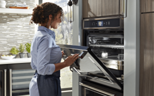 Woman opening an oven door and looking inside