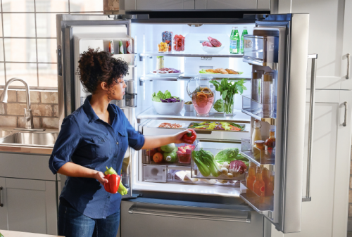 Woman selecting red and green peppers from a KitchenAid® French Door Refrigerator.