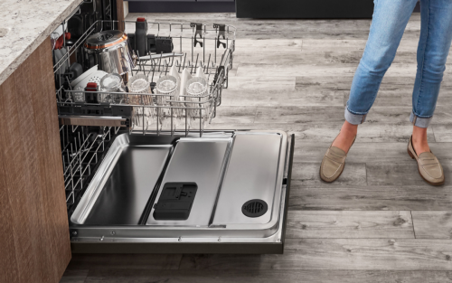 A woman standing next to an open KitchenAid® dishwasher in a modern kitchen