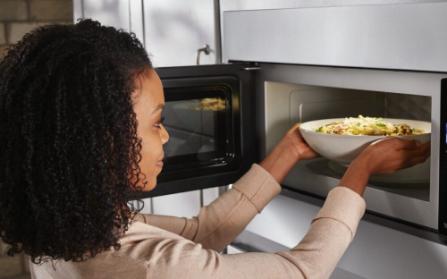 Person placing a bowl inside a built-in microwave