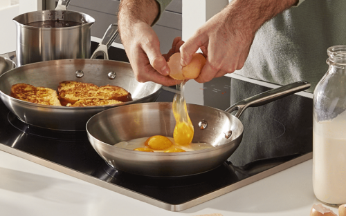 Eggs being cracked into a pan on the stove along with other items on the cooktop