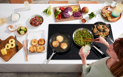 A person preparing various types of food on a KitchenAid® Cooktop