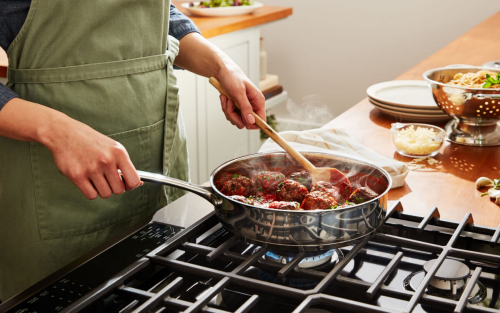 A person preparing food in a pan on a gas cooktop