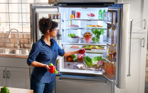 Person loading bell peppers into the crisper drawer of a refrigerator