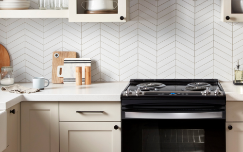 Black electric stove between cream cabinetry in front of a white herringbone backsplash