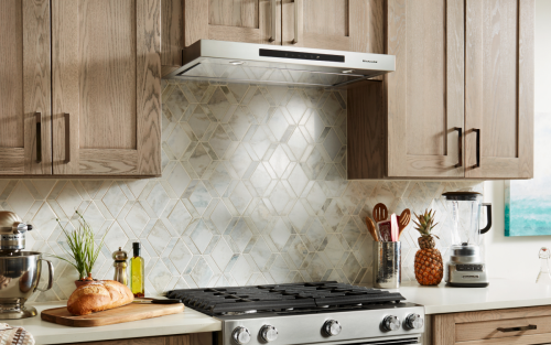 KitchenAid® range hood surrounded by light brown cabinetry