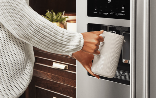 A person filling up a container at their refrigerator’s exterior ice and water dispenser