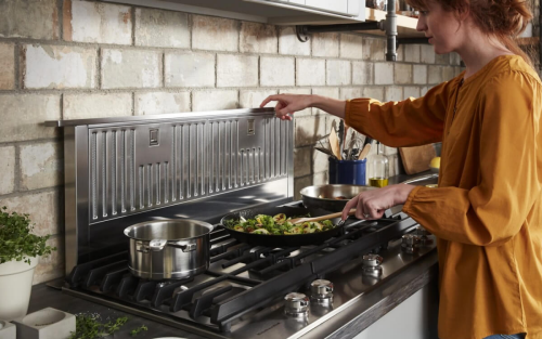 A closeup of a KitchenAid® gas cooktop with a person cooking food 