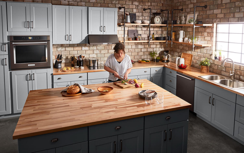 A person chopping vegetables at an island in a large, spacious kitchen