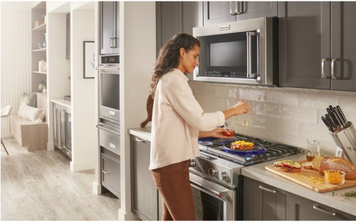 Person cooking on a stovetop with a KitchenAid® over-the-range microwave above