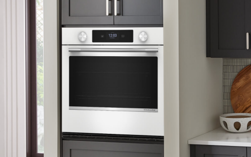 The interior of a kitchen with gray cabinetry, white countertops and a single wall oven