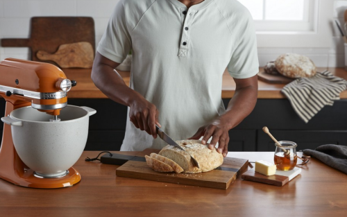 Person slicing a loaf of bread next to a KitchenAid® stand mixer