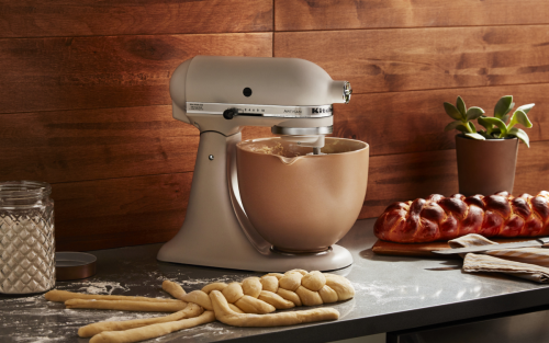 A white KitchenAid® stand mixer next to a loaf of homemade bread.