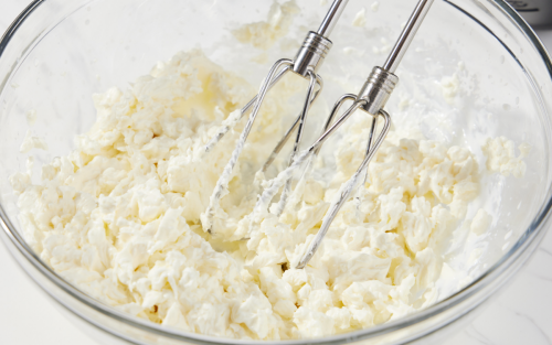 Hand mixer beaters in glass mixing bowl of creamed butter and sugar