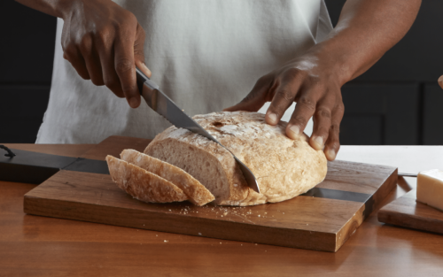 Man slicing fresh bread on countertop next to stand mixer