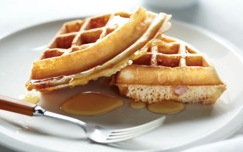 Homemade Belgian waffles on a plate with maple syrup.