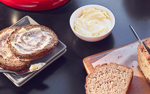 Cutting a loaf of wheat bread on the counter with butter nearby