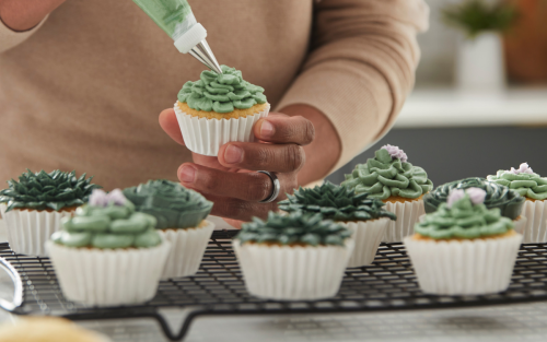 Person piping frosting onto a cupcake