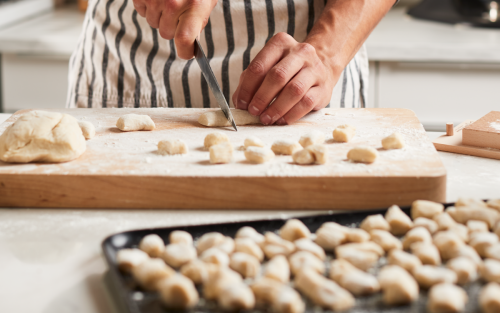 A man cutting pieces of potato gnocchi dough and placing them on a baking sheet in a modern kitchen. 