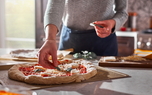 Person adding toppings to homemade pizza dough