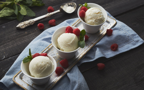 Individual bowls with scoops of vanilla ice cream and fresh raspberries on a table