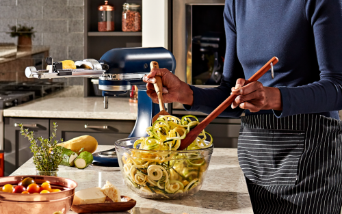 Woman tossing salad with veggie noodles in a glass salad bowl