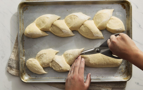 Person scoring bread on a baking sheet with kitchen scissors