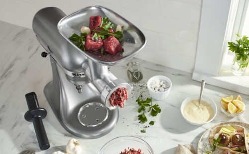 KitchenAid® Stand Mixer with food grinder attachment grinding meat on counter with ingredients