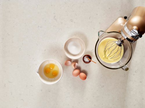 KitchenAid® stand mixer with whipped egg whites in the mixing bowl next to a bowl of cracked eggs and salt.