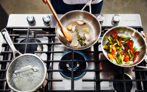 Gas stovetop with lit burner and several pots and pans sautéing food