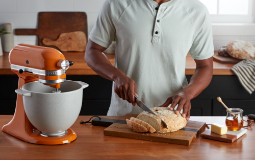 Person slicing bread next to an orange KitchenAid® stand mixer