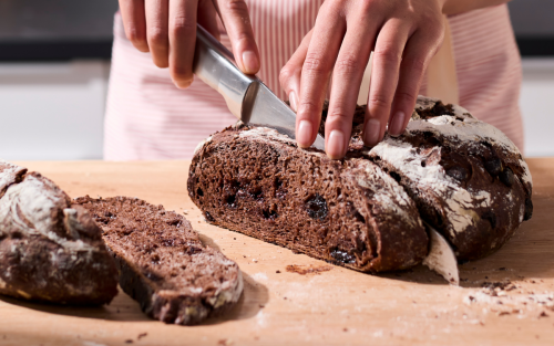 Person slicing dark brown bread