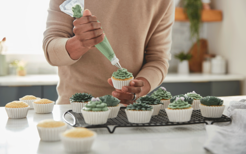 Person piping frosting onto a cupcake