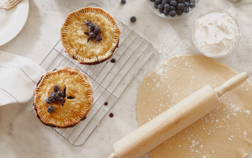 A blueberry pie next to a rolling pin and flour.