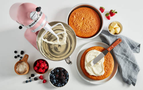 A KitchenAid® stand mixer with cake frosting next to a couple of baked cakes ready for frosting.