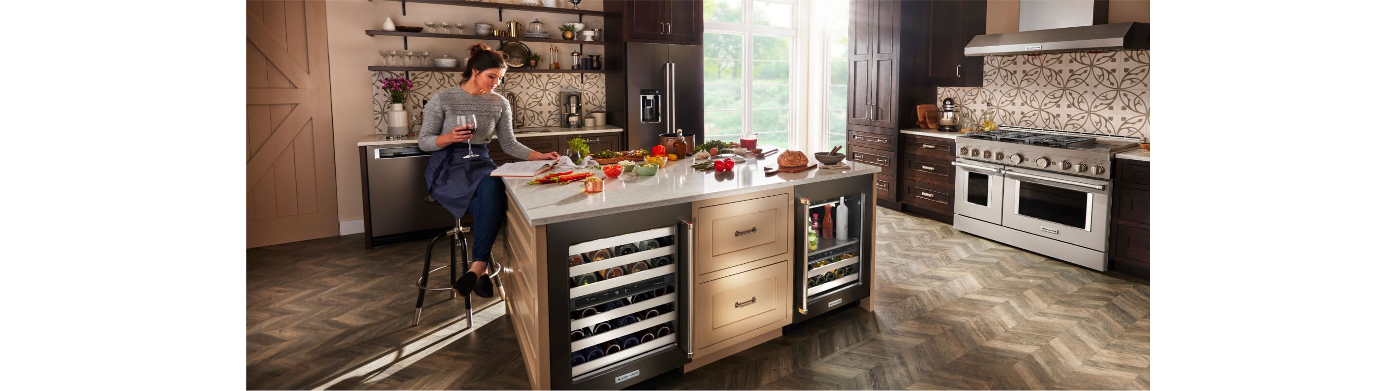 A person sitting at the island of a bold, modern kitchen, outfitted with a suite of KitchenAid® appliances.