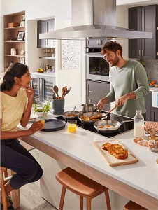 People in a kitchen cooking on an electric cooktop with a range hood above them