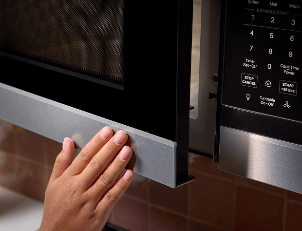 A person touching the exterior of a KitchenAid® microwave.