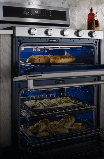 A large KitchenAid® double oven range cooking garlic bread, asparagus and whole chickens inside the oven