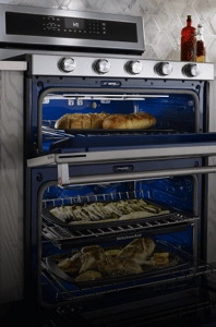 A large KitchenAid® double oven range cooking garlic bread, asparagus and whole chickens inside the oven