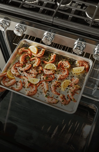 Sliced lemons and seasoned prawns on a baking dish inside of a range oven
