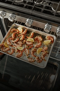 Sliced lemons and seasoned prawns on a baking dish inside of a range oven