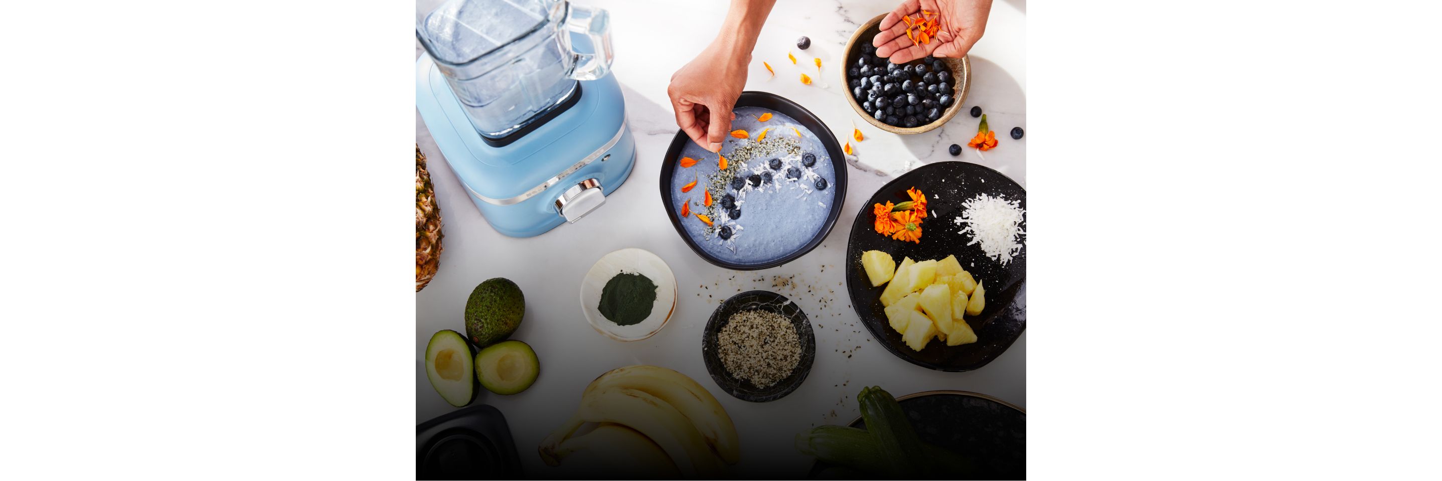 A person garnishing a blue smoothie bowl with fresh ingredients. 