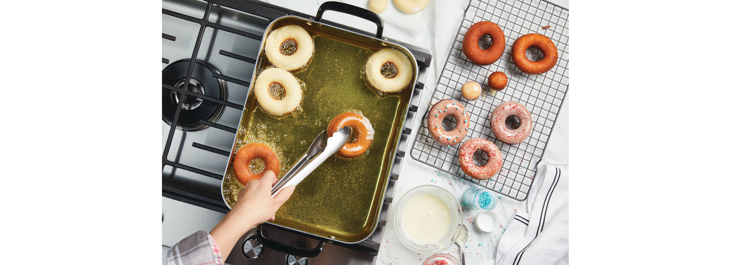 A person frying donuts in a KitchenAid® roasting pan filled with oil.