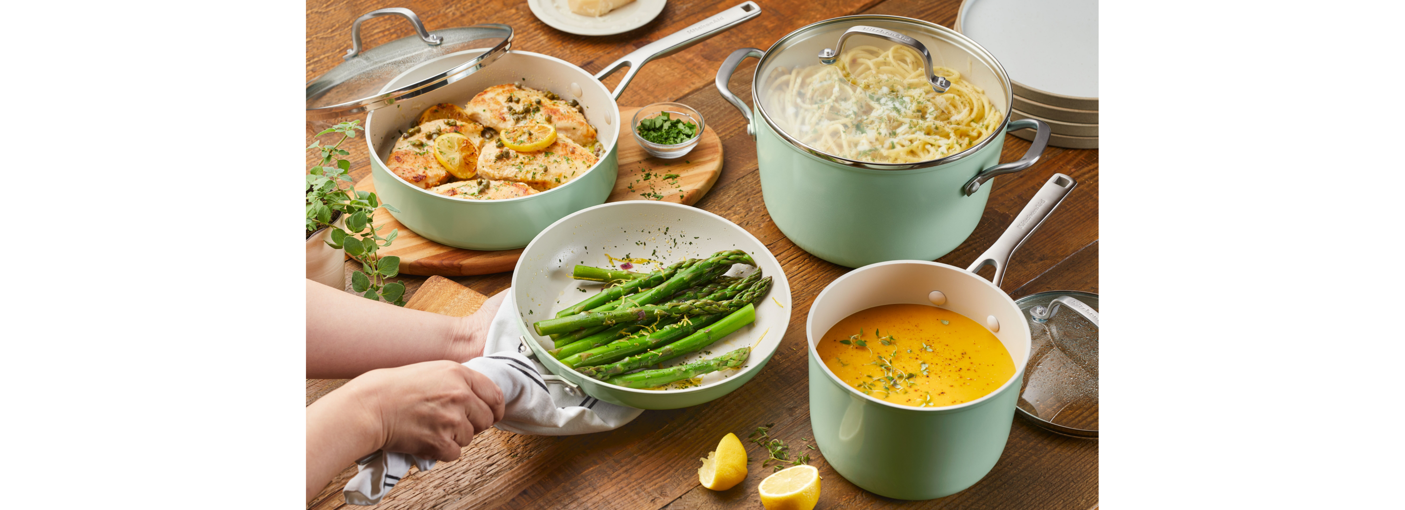 A person serving pasta, chicken, asparagus and a sauce in hard-anodized ceramic cookware.