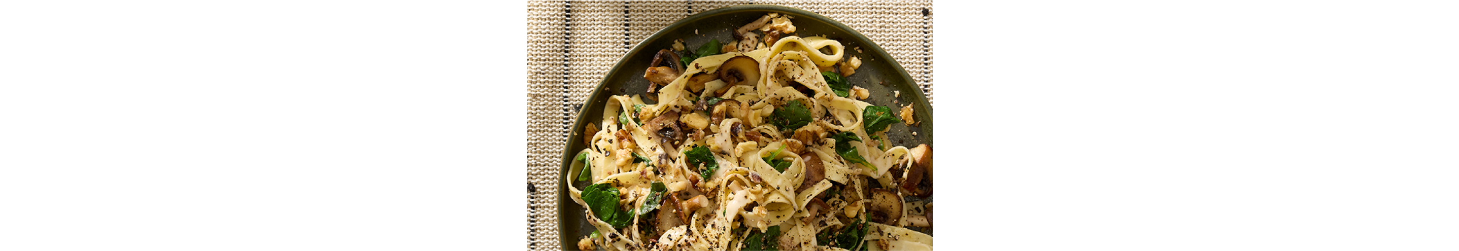 A plate of fresh fettuccine with mushrooms, greens and walnuts.