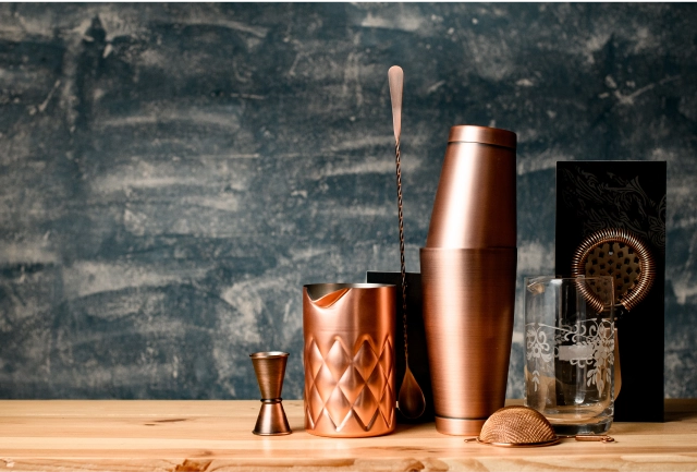 A set of copper cocktail shakers on a wooden counter.