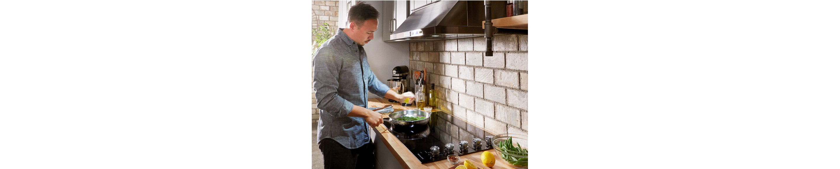A man squeezing a lemon in a pan of green beans on an induction cooktop.