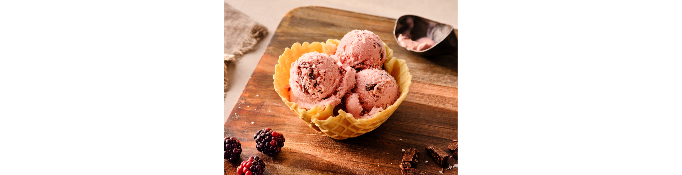Several scoops of pink blackberry ice cream in a waffle cone bowl.