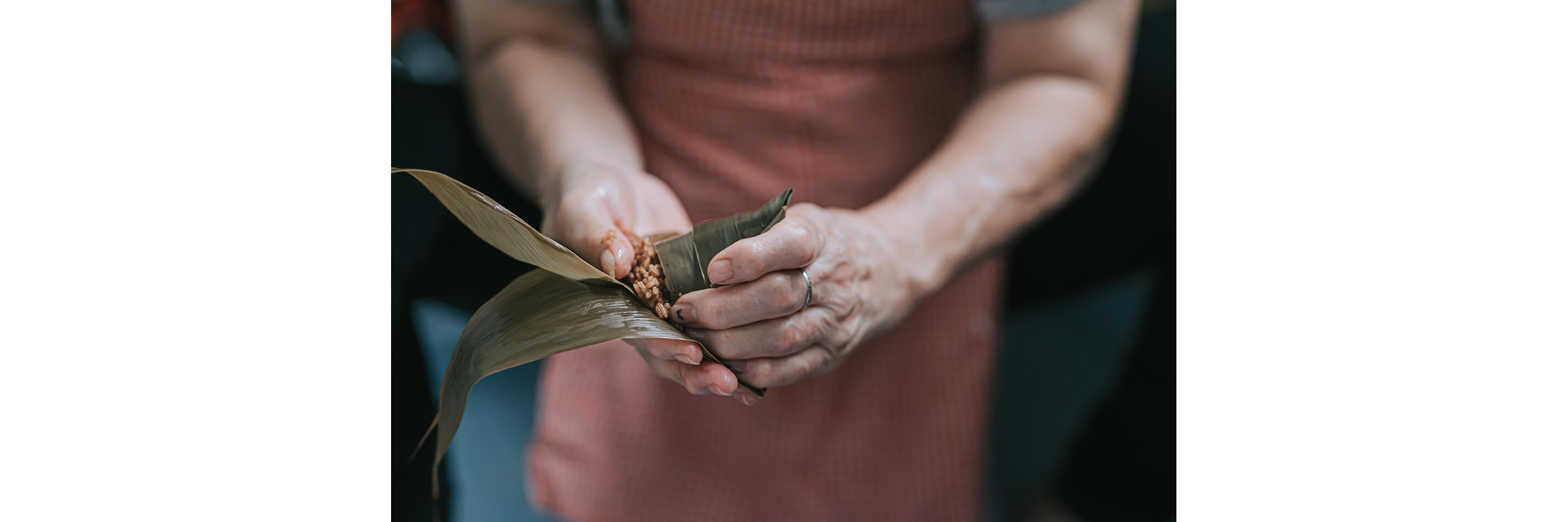 Expert hands gently wrapping rice in bamboo leaves.